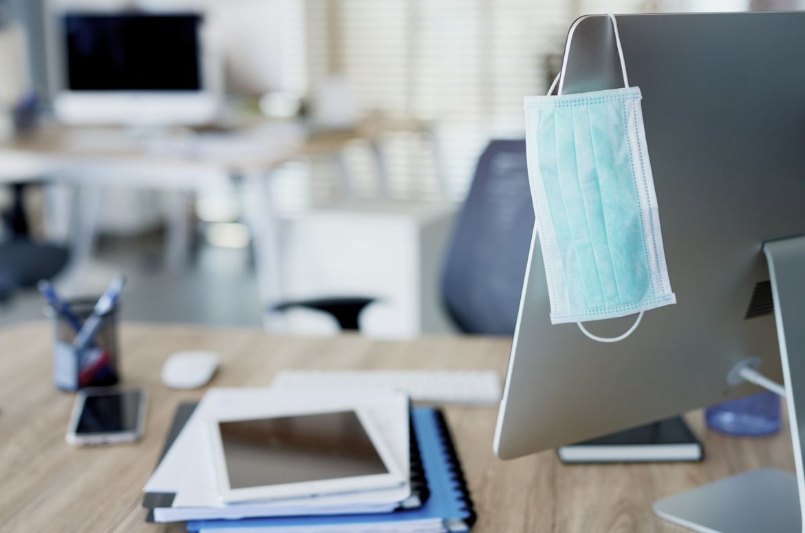 Face mask hanging on computer screen in an empty office min