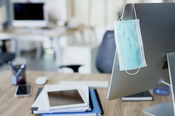 Face mask hanging on computer screen in an empty office min