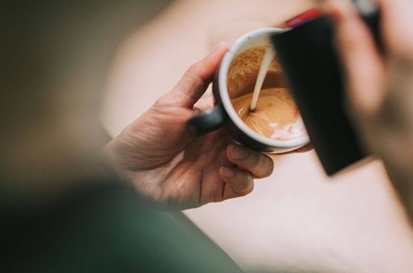 Over the shoulder barista pouring milk into coffee