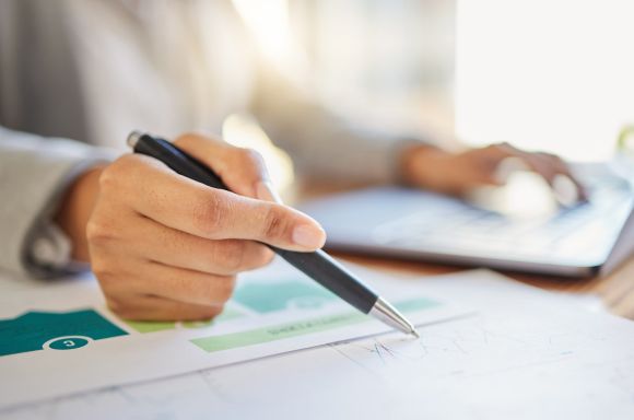Business man writing on financial graph with laptop