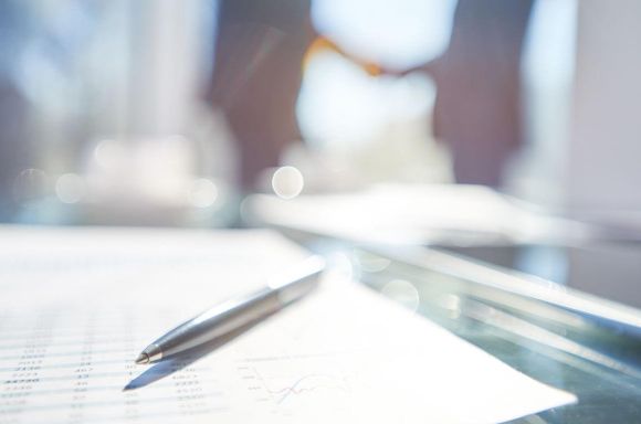 Two businessmen shaking hands behind financial documents