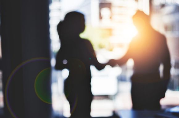 Man and woman shaking hands in a boardroom light shining through